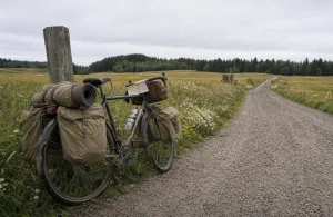 Lastad touringcykel lutad mot ett trästaket på en grusväg genom öppet landskap