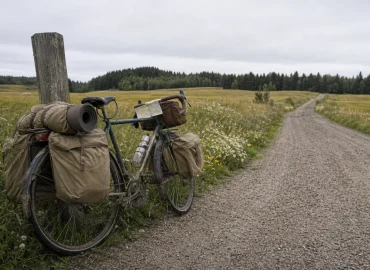 Lastad touringcykel lutad mot ett trästaket på en grusväg genom öppet landskap