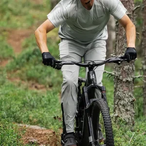 Cyklist i röd hjälm och röd tröja cyklar på muddig stig med elcykel genom uppodlat terräng, andra cyklister suddigt i bakgrunden.