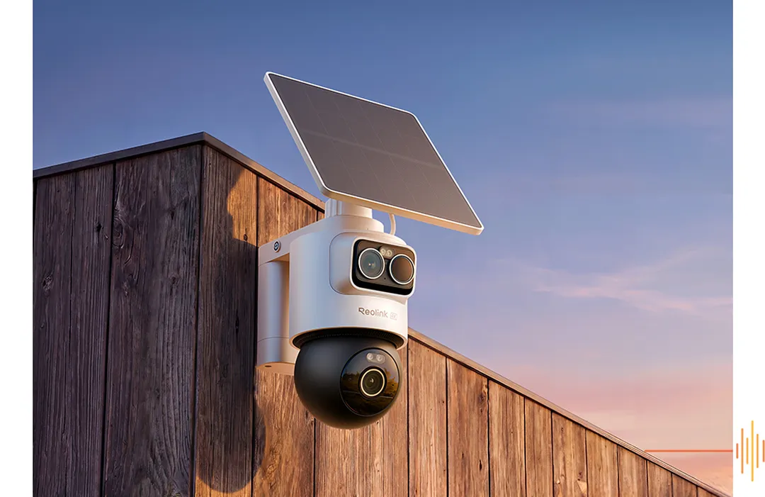 Reolink övervakningskamera med solpanel monterad på träbygnad mot blå himmel vid solnedgång.